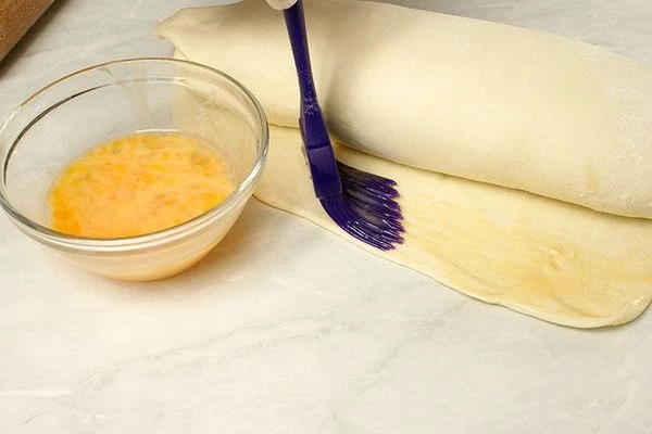 Край теста смазать яйцом и положить на противень, швом вниз.