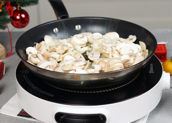 В сковороде на оливковом масле обжарить нарезанный репчатый лук и шампиньоны в течение 1-2 минут.