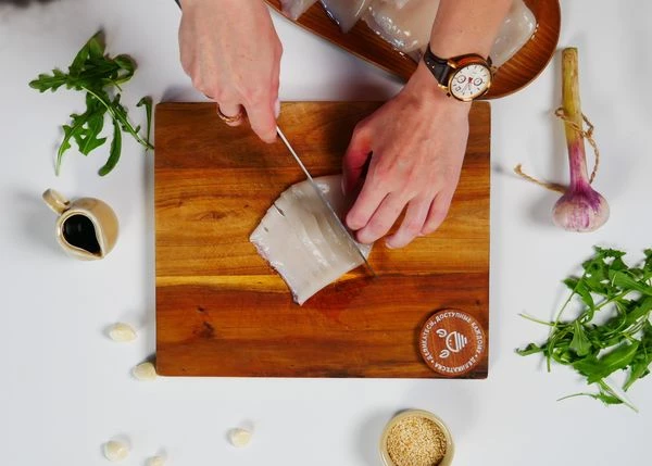 Кальмары разморозить на нижней полке холодильника. Очистить от пленки. Нарезать с верхней стороны на полоски, не прорезая нижнюю.