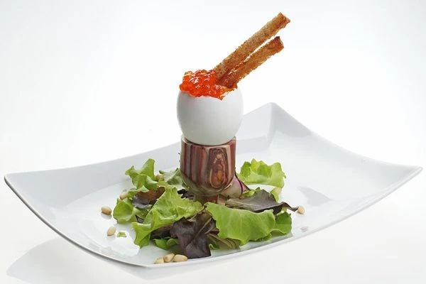 Готовое яйцо установите в подставку для яиц, аккуратно ножом удалите верхнюю часть скорлупы. Украсьте красной икрой, кедровыми орехами, подсушенными гренками и листьями салата.