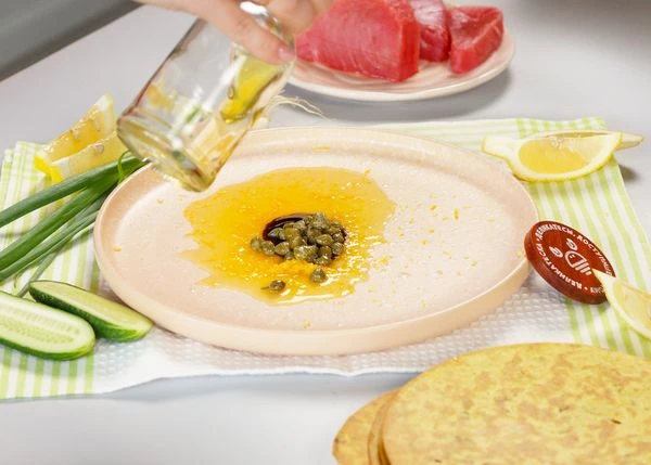 В тарелку для подачи налить масло, потереть цедру и выдавить сок лимона и апельсина. Добавить каперсы, устричный соус и соль. Перемешать.