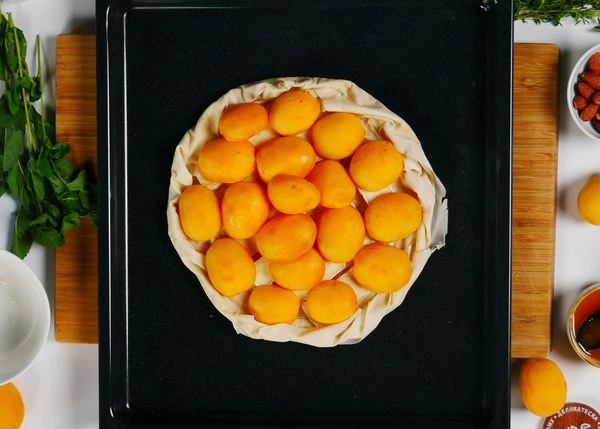 Завернуть края теста во внутрь. Разложить половинки абрикосов.