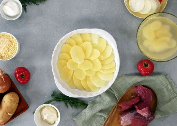 Картофель очистить, нарезать тонкими ломтиками. Выложить в форму для запекания. 