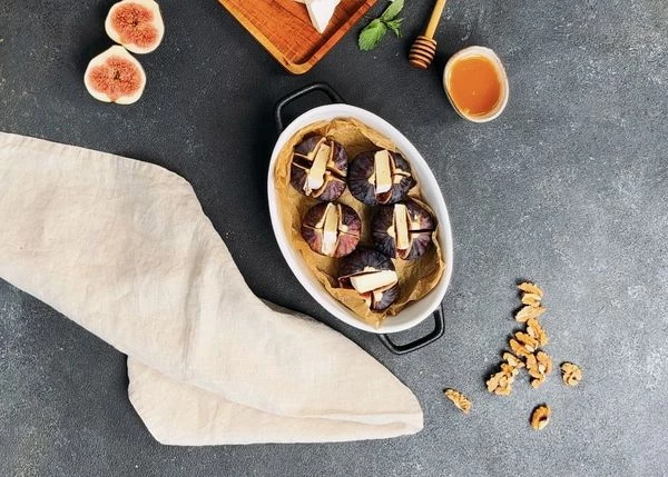 Выложить инжир в емкость для запекания, застеленный пергаментом. Равномерно распределить кусочки камамбера в половинках инжира. 