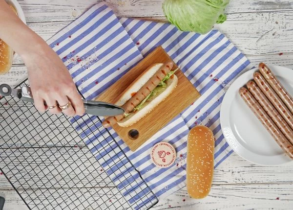 Булочку для бургера смазать кетчупом. Затем выложить нарезанный айсберг и обжаренную колбаску.