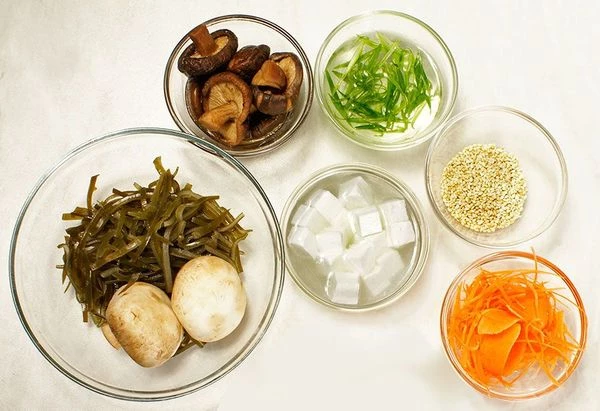 Водоросли вакаме или морскую капусту размочить в холодной кипяченой воде 15-20 минут. Морковь и лук зеленый нарезать тонкой соломкой. Творог тофу нарезать небольшими кубиками. Грибы шиитаки размочить в теплой воде 1-2 часа, затем слить воду, залить свежей водой и проварить 20-30 минут. Грибы шампиньоны промыть и нарезать тонкими пластиками.