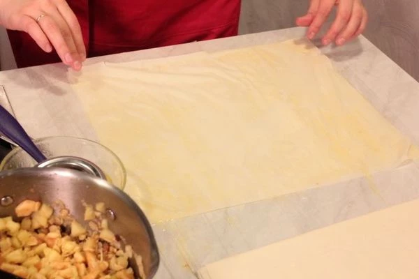 Тесто Фило аккуратно развернуть. На стол натянуть пищевую пленку, выложить один лист теста, смазать всю поверхность растопленным сливочным маслом, сверху уложить еще один лист теста, еще раз смазать маслом.