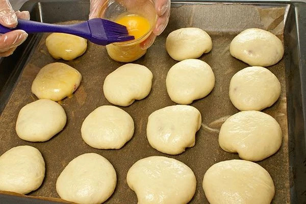 Выложить пирожки на противень, выстеленный пергаментной бумагой, смазать желтком. Дать постоять 5-7 минут для подъема.