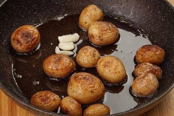 Пока рыба маринуется, обжарить картофель черри на смеси растительного и сливочного масла и парой долек чеснока.