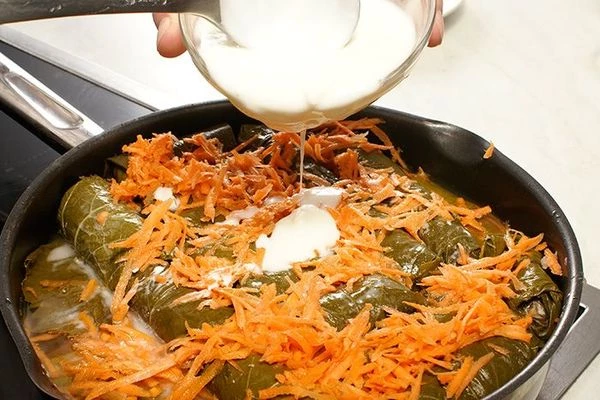 Сметану или натуральный йогурт смешать с тертым чесноком и влить в долму, потушить еще 5-10 минут.