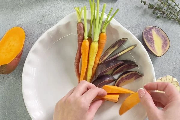 Овощи вымыть. Батат и картофель нарезать дольками. В форму для запекания выложить молодую морковь, нарезанный батат, картофель.