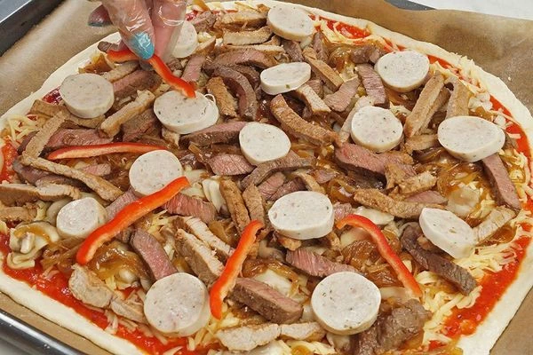 Сверху на лук уложите мясную начинку (свинину, говядину, купаты). Украсьте нарезанным перцем.