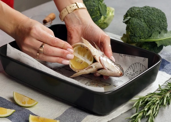 Рыбу разморозить на нижней полке холодильника. Извлечь из пакета. Вложить в брюшко половинку лимона.