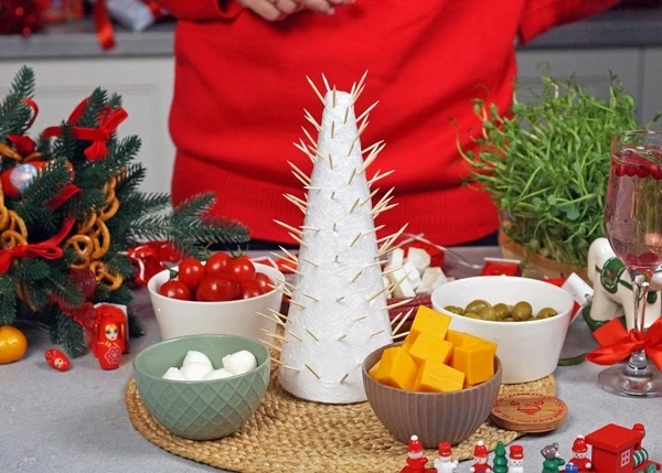 Сыры нарезать на кусочки. Пенопластовый конус завернуть в пищевую пленку. Воткнуть зубочистки по всему периметру.