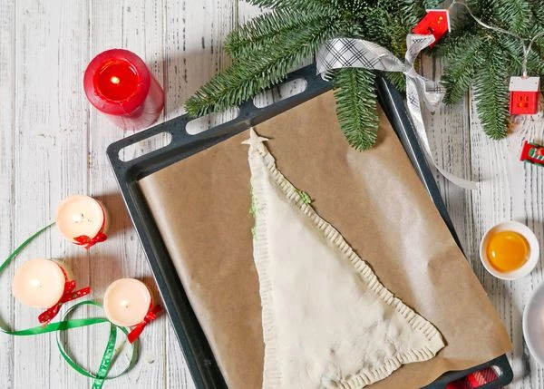 Сверху выложить второй треугольник теста. Примять края вилкой. Вырезать из остатков теста звезду. Выложить на макушку ёлочки.