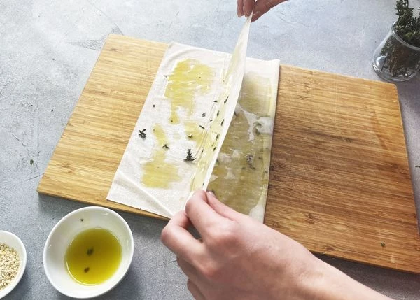 Тесто фило разморозить. Один лист теста выложить на доску, посыпать листиками тимьяна смазать маслом, свернуть пополам.