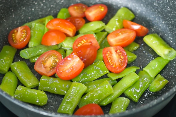 Фасоль разморозить. Томаты черри и оливки нарезать пополам.
В сковороду налить вторую половину масла, выложить фасоль, жарить пару минут, затем добавить томаты черри, соль, молотый перец и томить еще пару минут.
