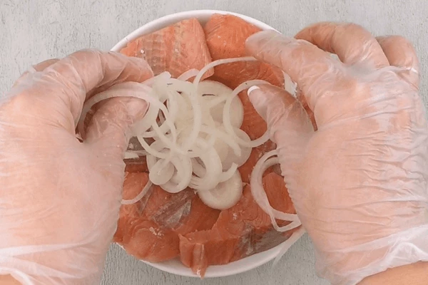 На картофель уложить филе рыбы, посолить, поперчить по вкусу.  Выложить тонкие колечки лука