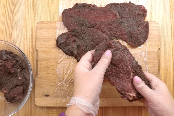 Подготовленное мясо разложить на пищевой пленке в один слой, прямоугольником, чтобы можно было завернуть в рулет.  Если какие то кусочки получились толстоваты, еще раз отбить их. 