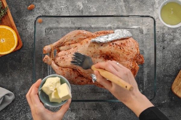 Ножки и крылышки обернуть фольгой. Переложить в форму для запекания, смазать утку мягким сливочным маслом.