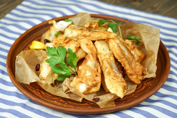 Готовую рыбу в кляре украсить зеленью и дольками лимона.