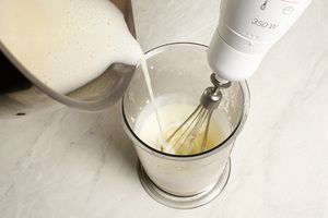 Растворенный желатин с молоком влить тонкой струйкой в йогуртную смесь, не переставая взбивать.